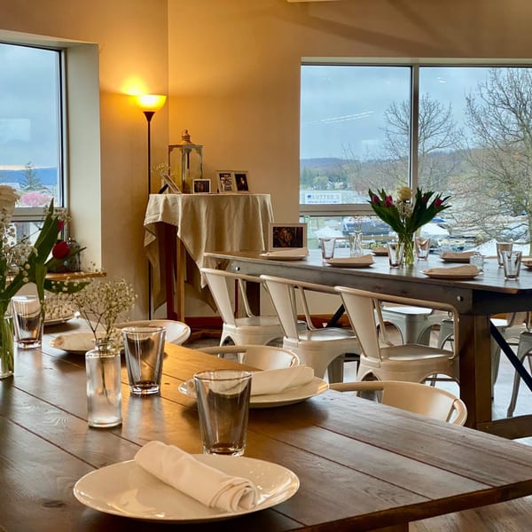 COHO Pizza & Wine Bar dining room with set tables, white chairs, and large windows overlooking Canandaigua Lake.