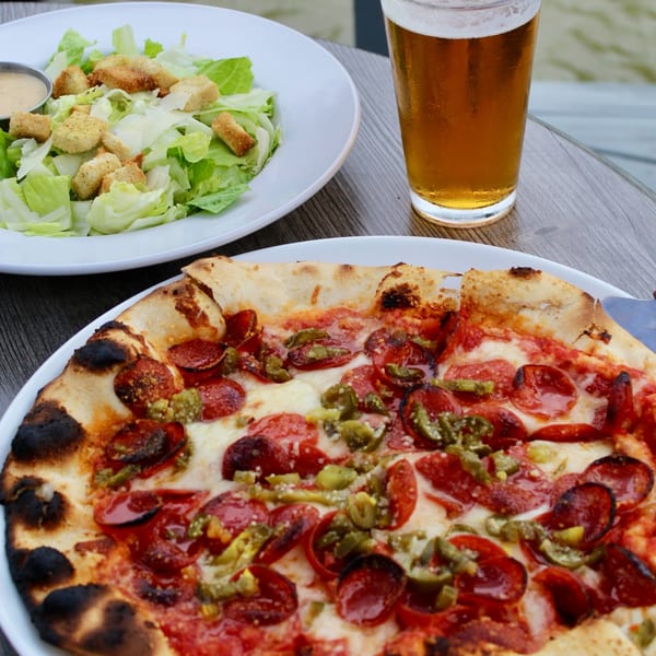 COHO Pizza & Wine Bar's pepperoni and jalapeño pizza, Caesar salad, and a beer on a wooden table.