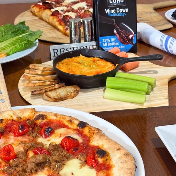 COHO Pizza & Wine Bar table with two pizzas, dip, bread, vegetables, and a "Wine Down Wednesdays" sign.