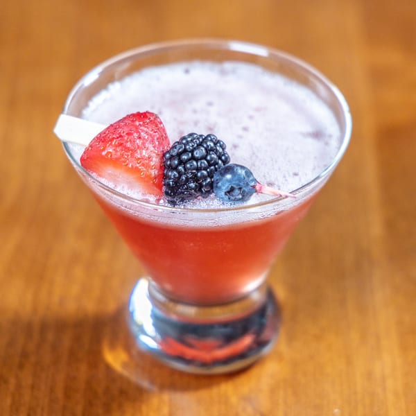 A COHO Pizza & Wine Bar cocktail, garnished with a strawberry, blackberry, and blueberry.