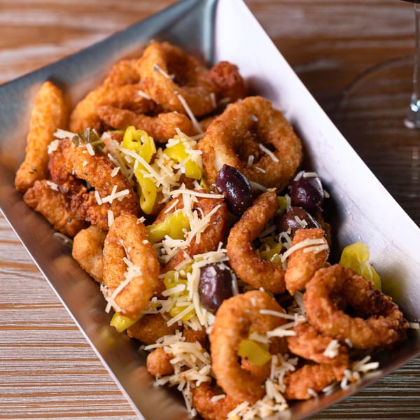 Fried calamari and banana peppers topped with shredded cheese and olives in a metal tray.