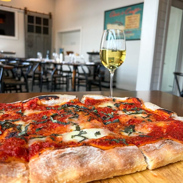 COHO Pizza & Wine Bar's Margherita pizza and a glass of white wine on a wooden table.