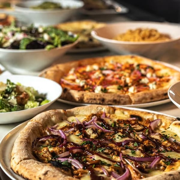 Two COHO pizzas, one with BBQ chicken and red onions, alongside salads and pasta.
