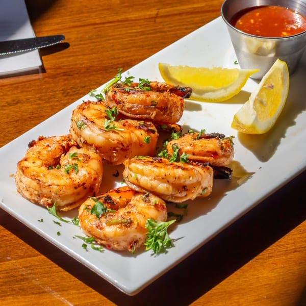 Grilled shrimp appetizer with parsley, lemon wedges, and a side of red dipping sauce.
