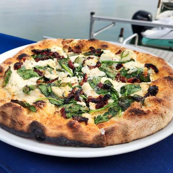 COHO Pizza with spinach, sun-dried tomatoes, and cheese on a white plate by Canandaigua Lake.