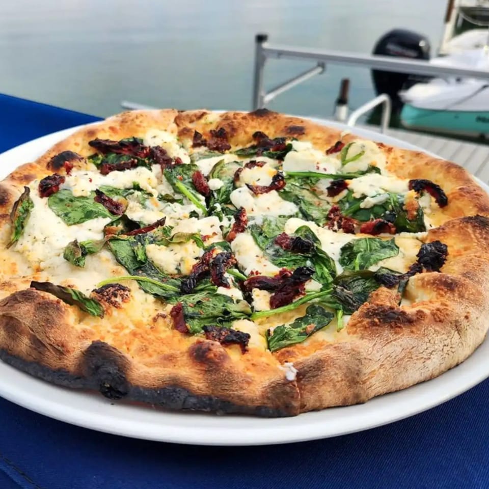 COHO Pizza with spinach, sun-dried tomatoes, and cheese on a white plate by Canandaigua Lake.