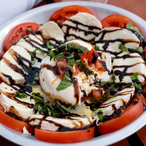 Caprese salad with sliced tomatoes, mozzarella, fresh basil, and balsamic glaze on a white plate.