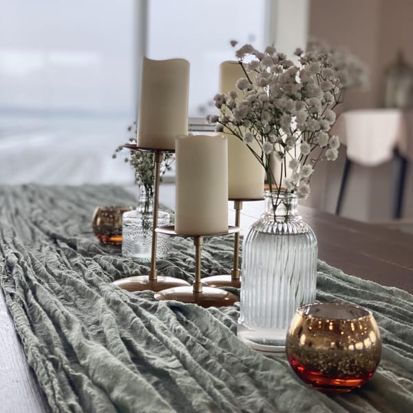 Candles, baby's breath, and votives on a grey table runner, with a lake view in the background.