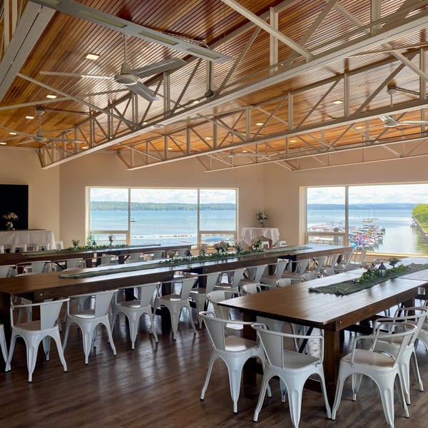 COHO Pizza & Wine Bar's dining room with long wooden tables, white chairs, and lake views.