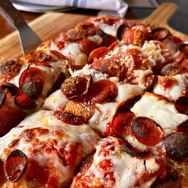 Close-up of a COHO pepperoni pizza with crispy edges and melted cheese on a wooden board.