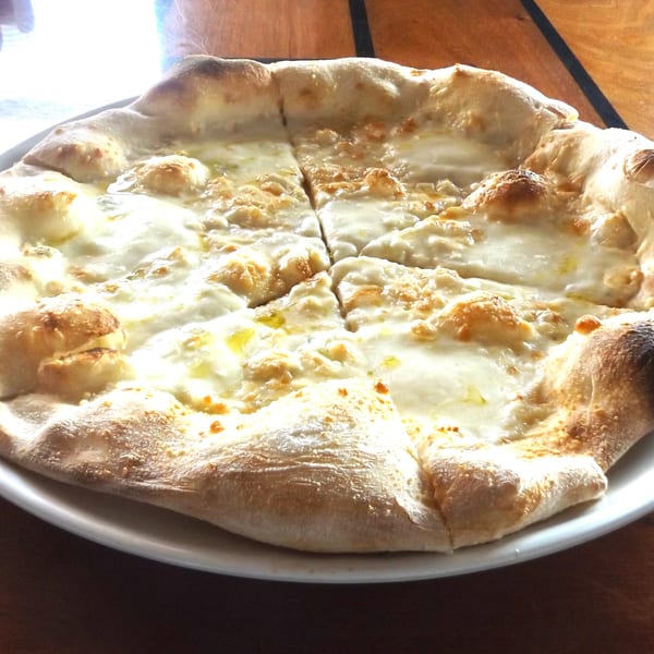 A freshly baked COHO Pizza, topped with melted white cheese and a golden crust, on a white plate.