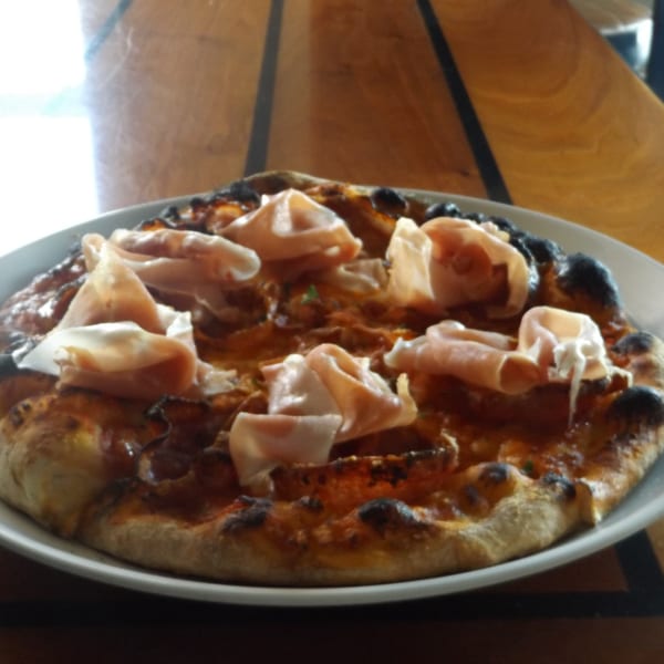 COHO Pizza & Wine Bar's pizza with prosciutto, tomato sauce, and charred crust on a white plate.