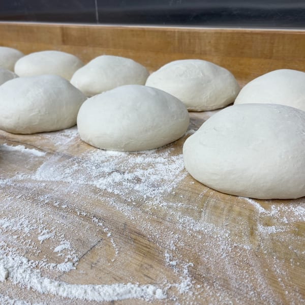 Rows of COHO Pizza dough balls resting on a floured wooden surface, ready for baking.