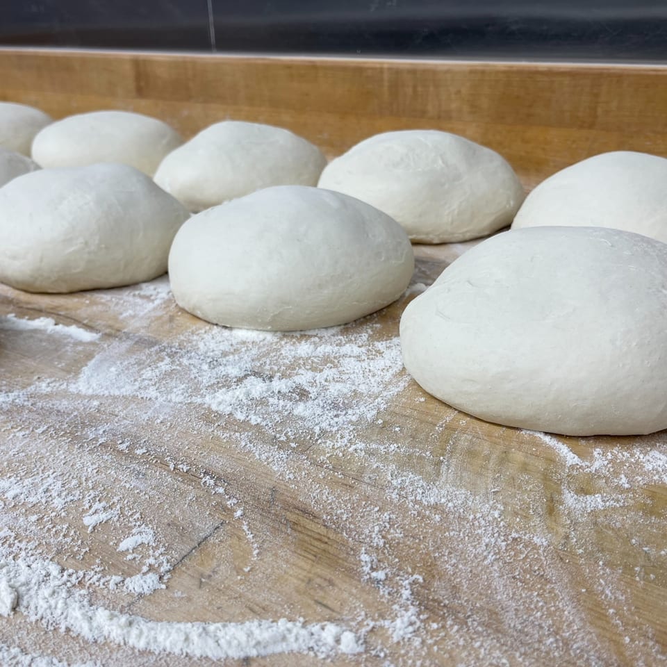 Rows of COHO Pizza dough balls resting on a floured wooden surface, ready for baking.