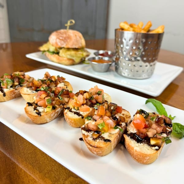 Bruschetta with tomatoes and balsamic glaze, with a burger and fries in the background.