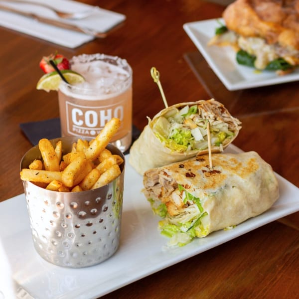 COHO Pizza & Wine Bar wraps with fries and a cocktail on a wooden table.